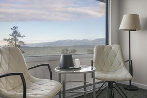 Une chambre d’hôtel avec deux fauteuils en cuir, une petite table avec une lampe et une vue sur les montagnes, visible à travers de grandes fenêtres.