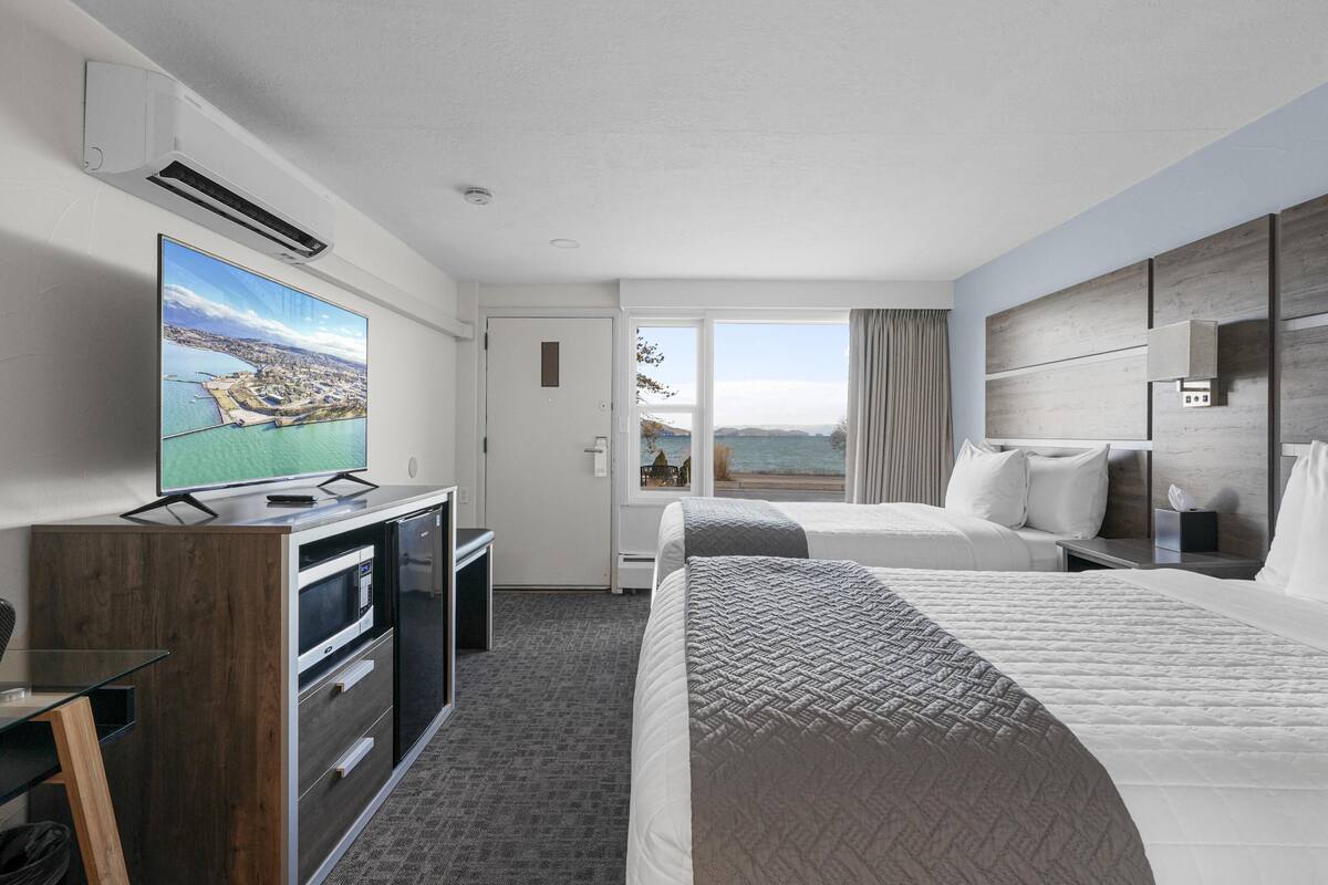 A hotel room with a large TV, a desk with a computer, two beds, and a view of the sea.