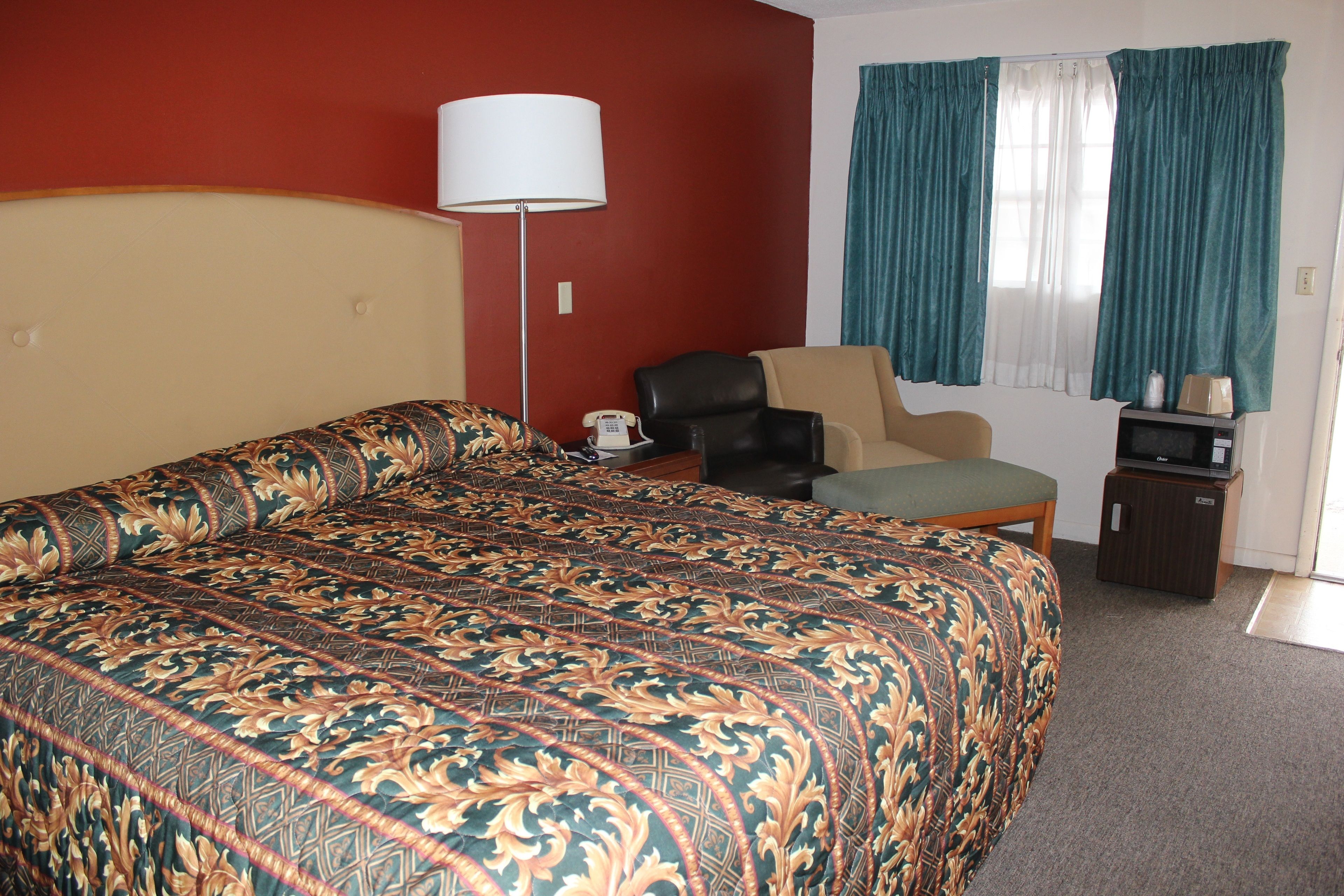 A hotel room with a large bed, a desk with a lamp, a chair, a television, and curtains.