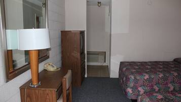 Une chambre d’hôtel équipée d’un bureau, d’un téléphone, d’un miroir, d’une armoire, d’un lit avec une couvre-lit à motifs floraux et d’une porte donnant sur une salle de bain.