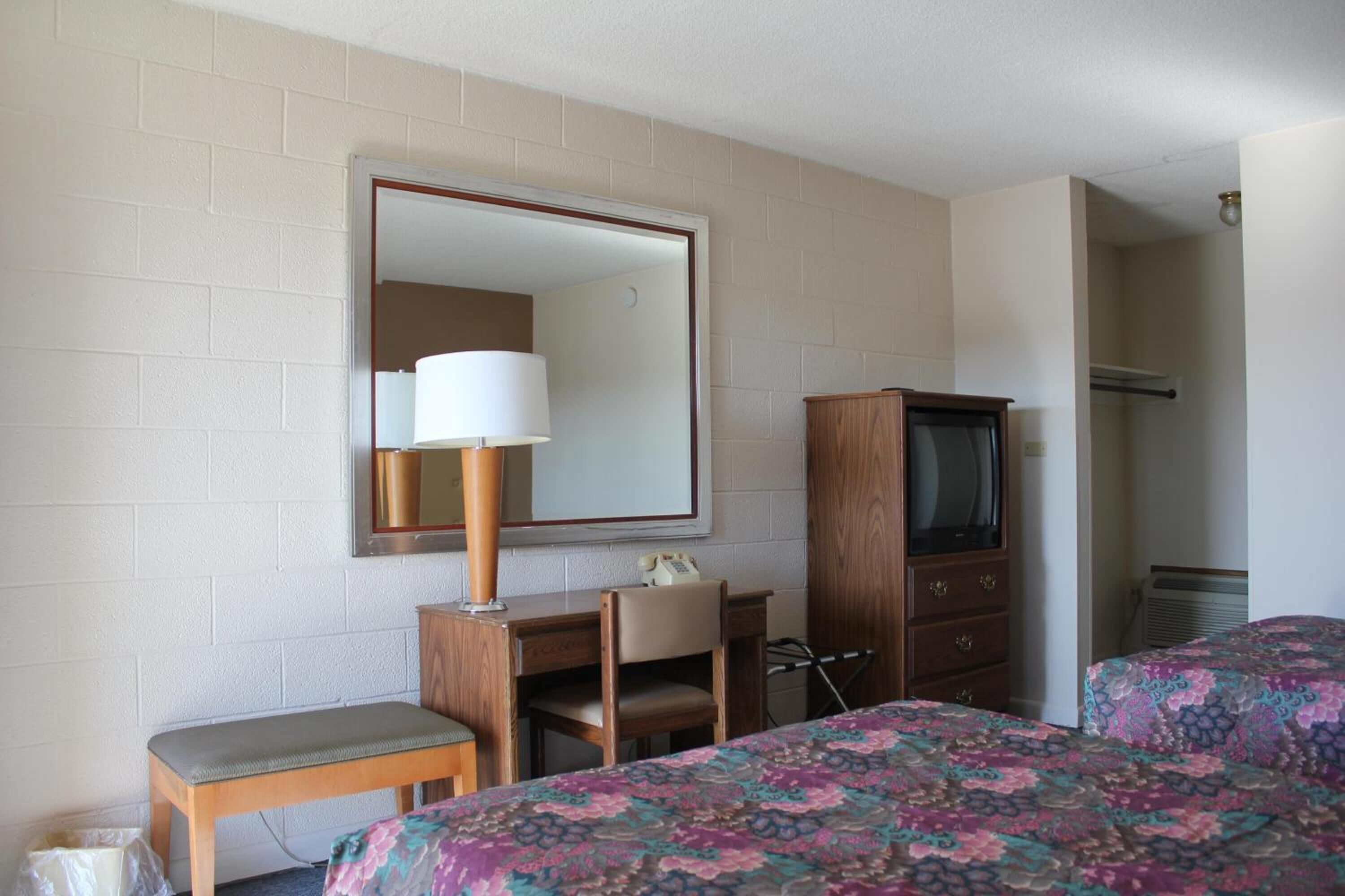 Una habitación de hotel con una cama, un escritorio con lámpara, un televisor y un armario.