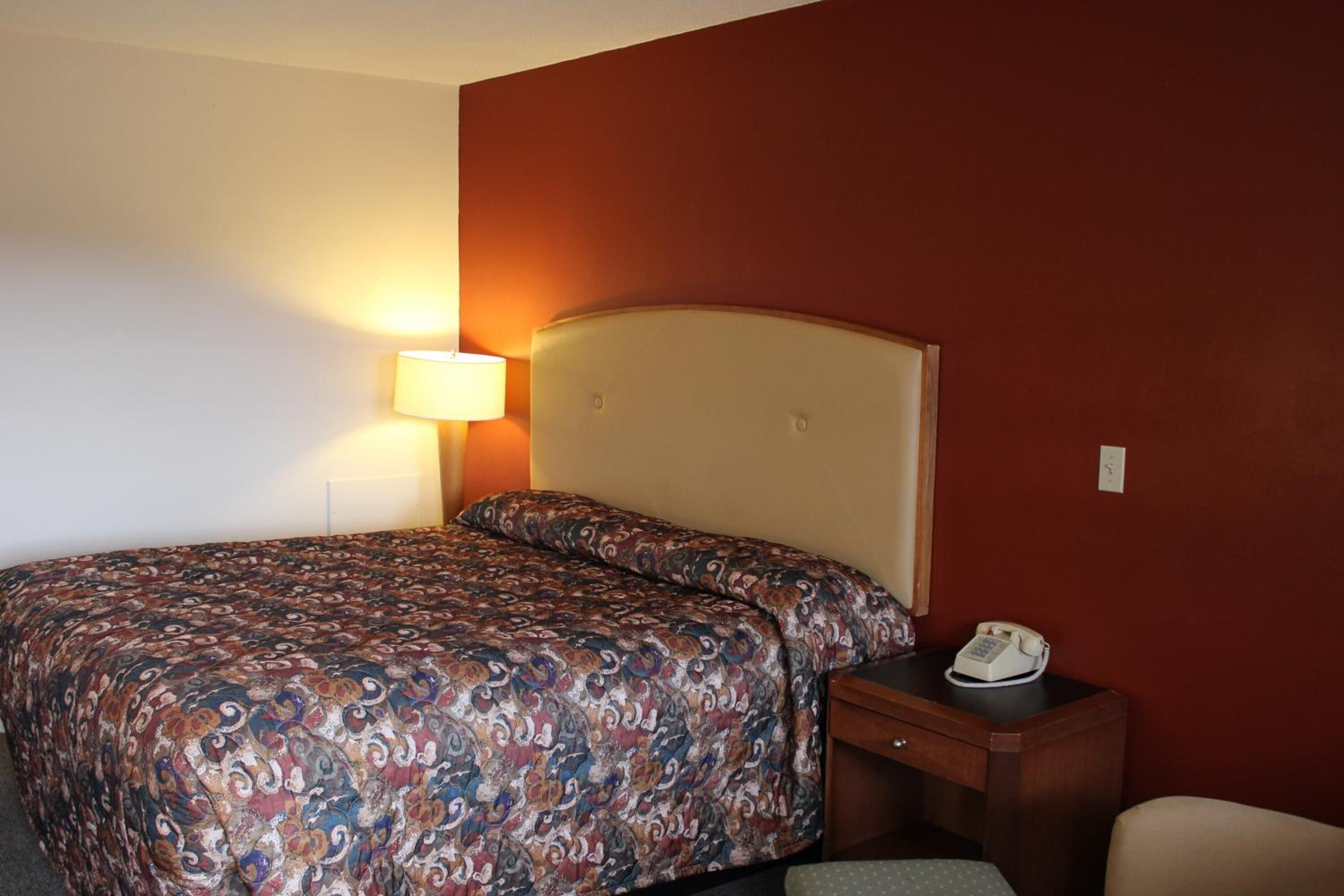 A hotel room with a bed, a bedside lamp, a telephone, and a chair.
