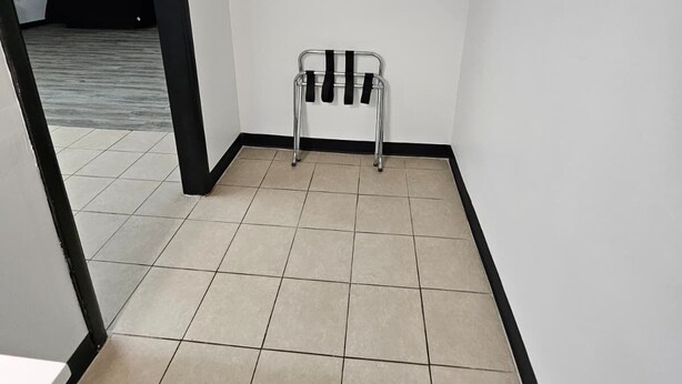 Habitación de esquina con suelo de baldosas, una silla de metal y una pared blanca con zócalo negro.