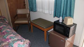 Una habitación de hotel con una cama, una silla, una mesita, un microondas y un refrigerador.