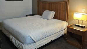 Una cama bien hecha en una habitación de hotel con cabecera de madera, una mesita de noche con lámpara y un cuadro en la pared.