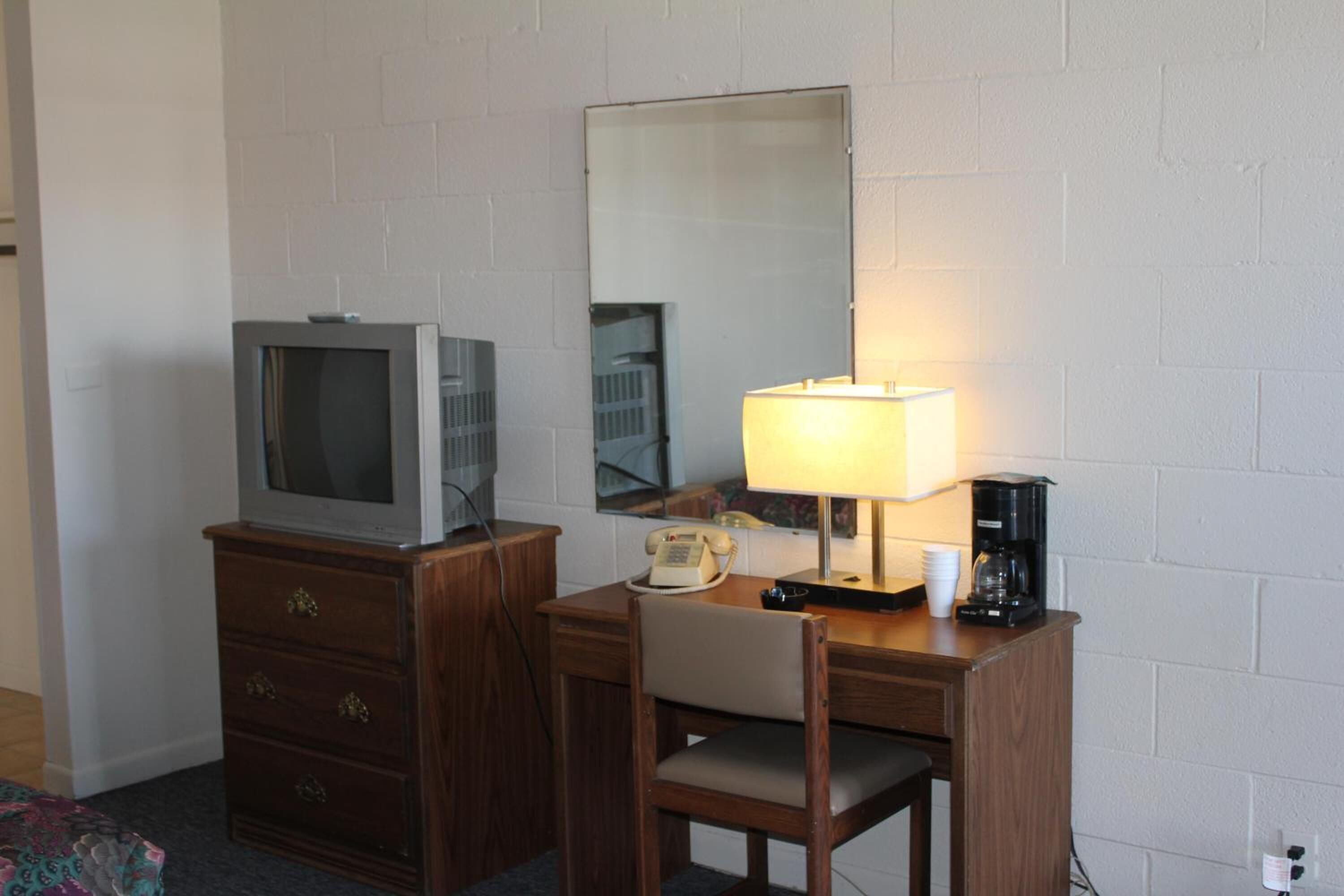 Une chambre d’hôtel équipée d’un bureau en bois, d’une télévision, d’une lampe, d’un téléphone et d’une machine à café.