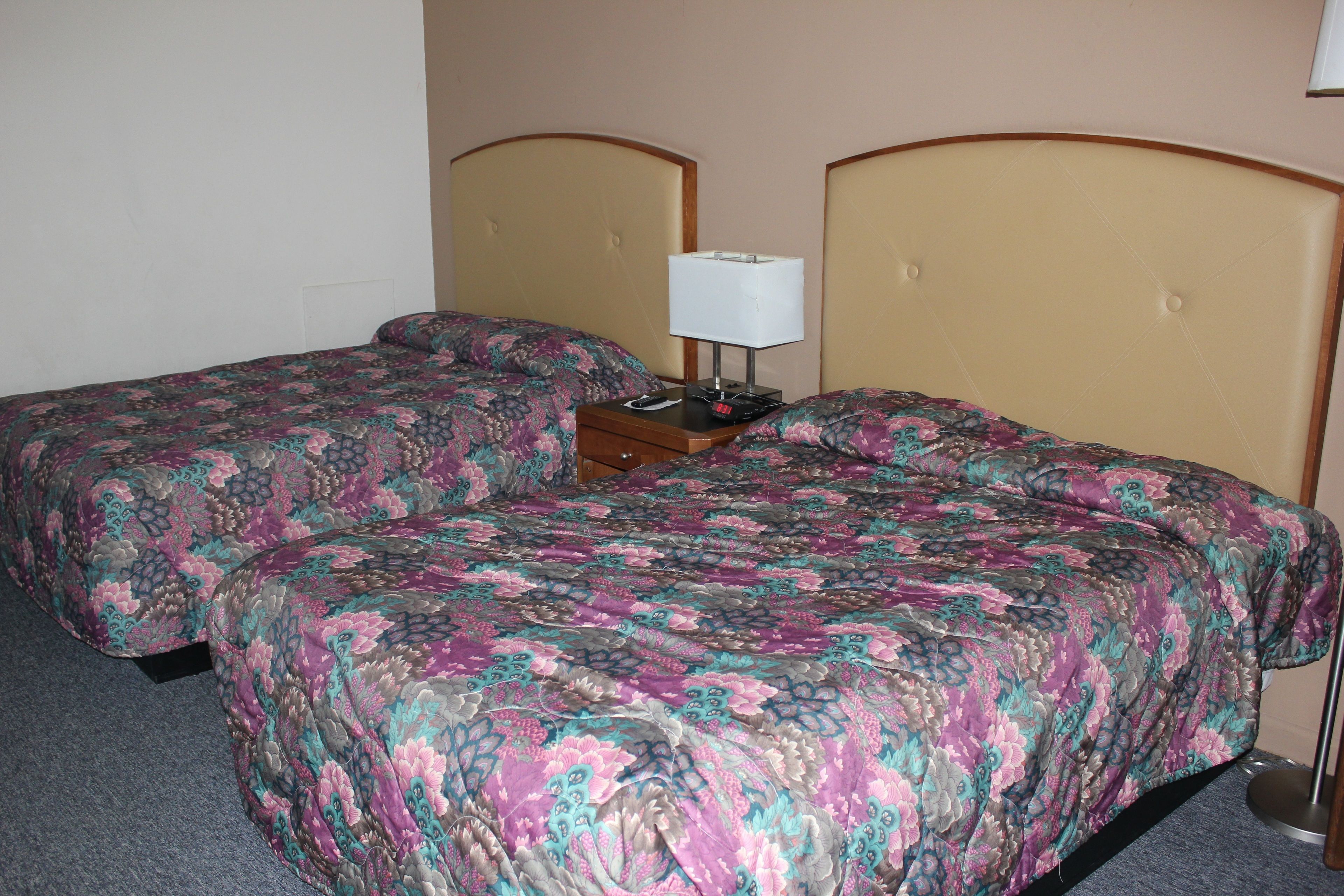 Una habitación de hotel con dos camas, cada una con una colcha de motivos florales, una mesita de noche con una lámpara y una lámpara de pared.