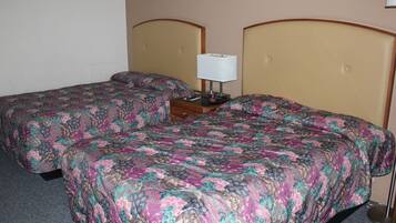Una habitación de hotel con dos camas, cada una con una colcha de motivos florales, una mesita de noche con una lámpara y una lámpara de pared.
