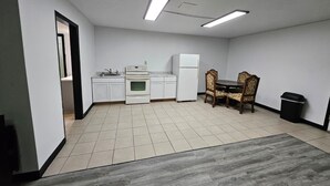 Cocina compacta con armarios blancos, estufa, refrigerador y comedor con mesa y sillas.