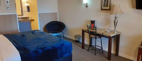A hotel room with a bed, a desk with a chair, a lamp, and a picture on the wall.