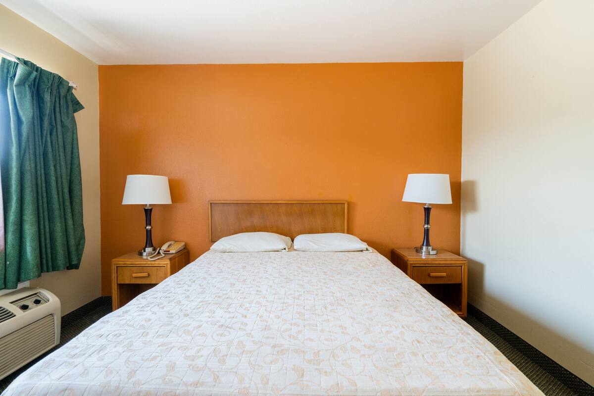 A hotel room with a large bed, two bedside tables with lamps, a telephone, and a heater.