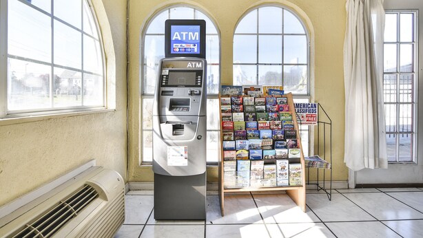 An ATM machine, a magazine rack, and large arched windows in a room with a tiled floor. - OYO Hotel Shreveport Airport North (Shreveport)