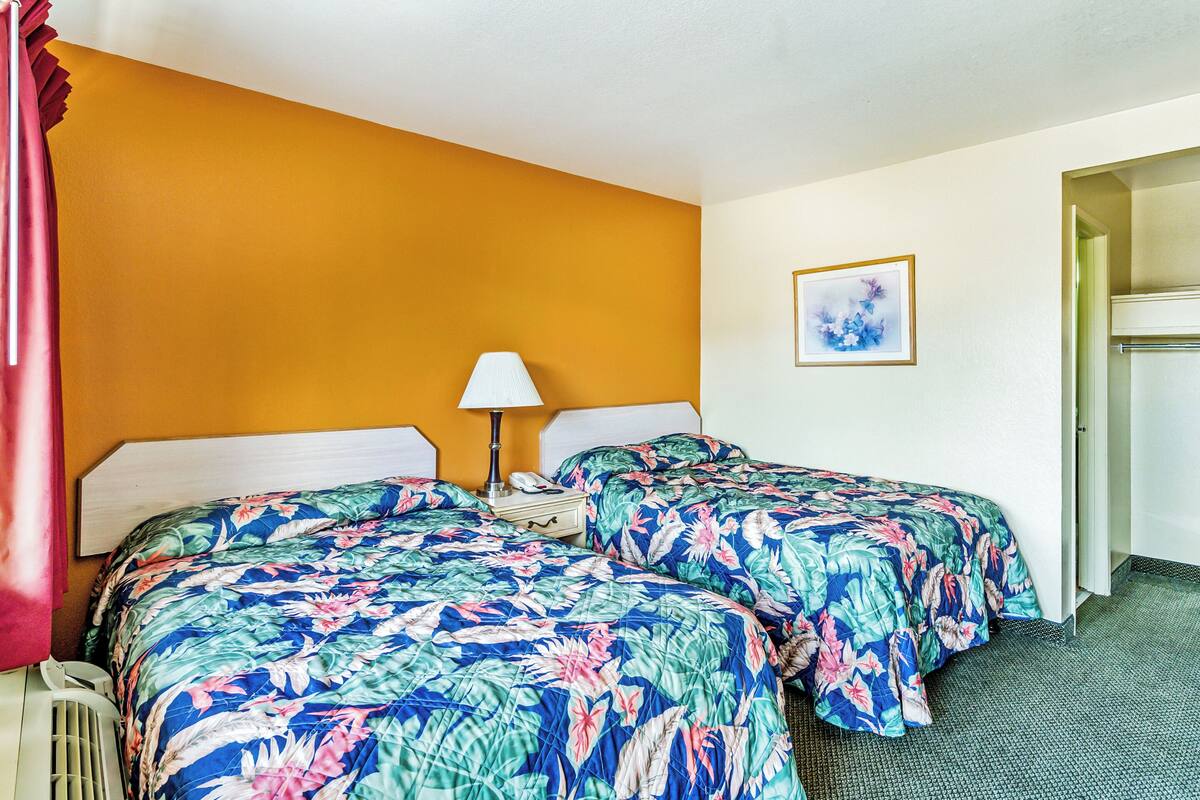 A hotel room with two beds, a nightstand, a lamp, and a painting on the wall.
