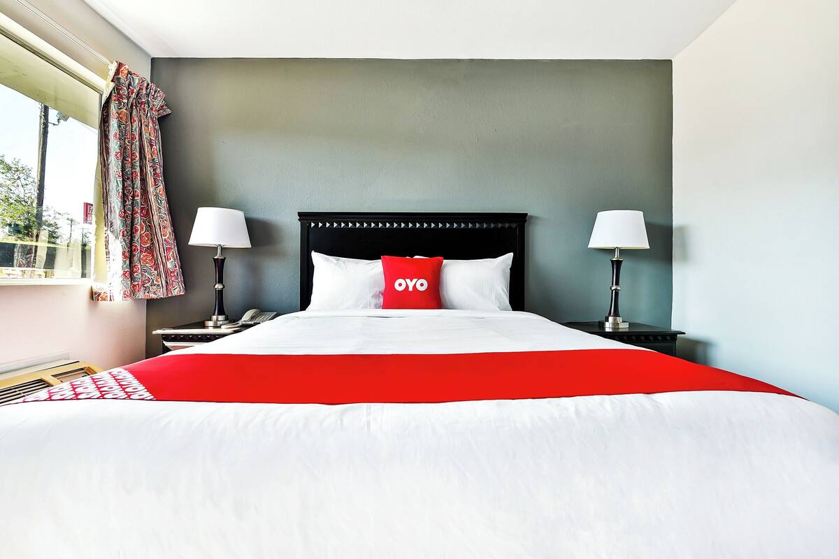 A hotel room with a large bed, two bedside lamps, a nightstand, a window with curtains, and a view of the outside.