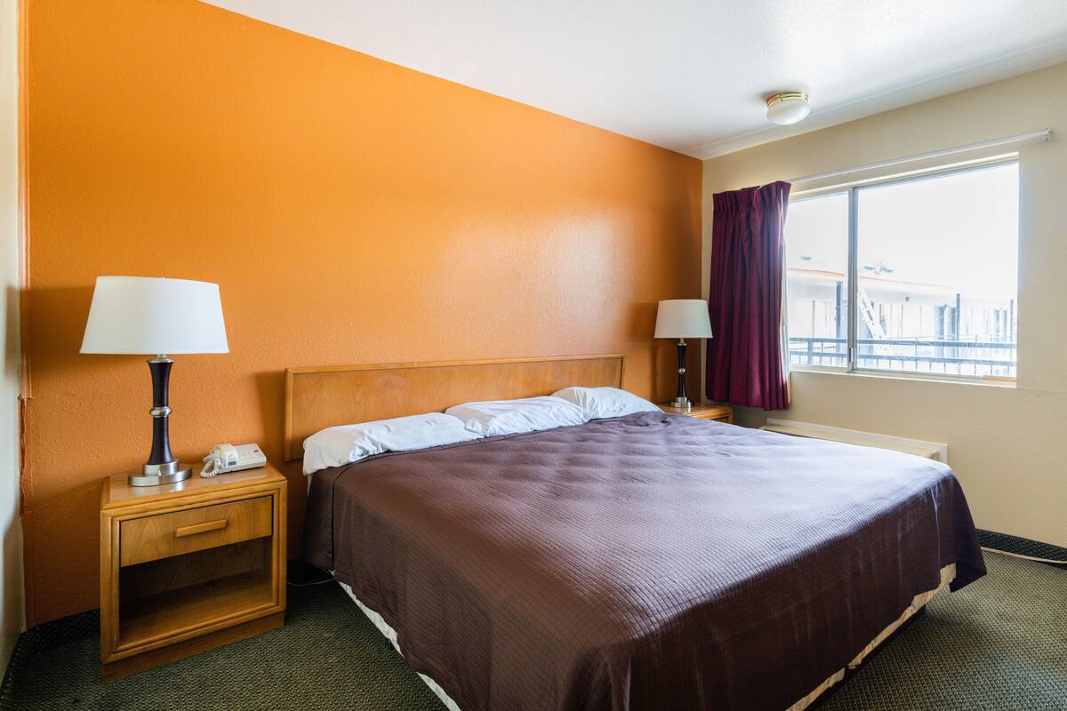 A hotel room with a large bed, two bedside tables with lamps, a window with curtains, and a view of a building outside.