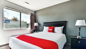 A hotel room with a large bed, a nightstand, a lamp, and a window with curtains. - OYO Hotel Shreveport Airport North (Shreveport)