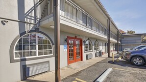 A building with a red door, a handicap accessible sign, and a parking area with a damaged car. - OYO Hotel Shreveport Airport North (Shreveport)
