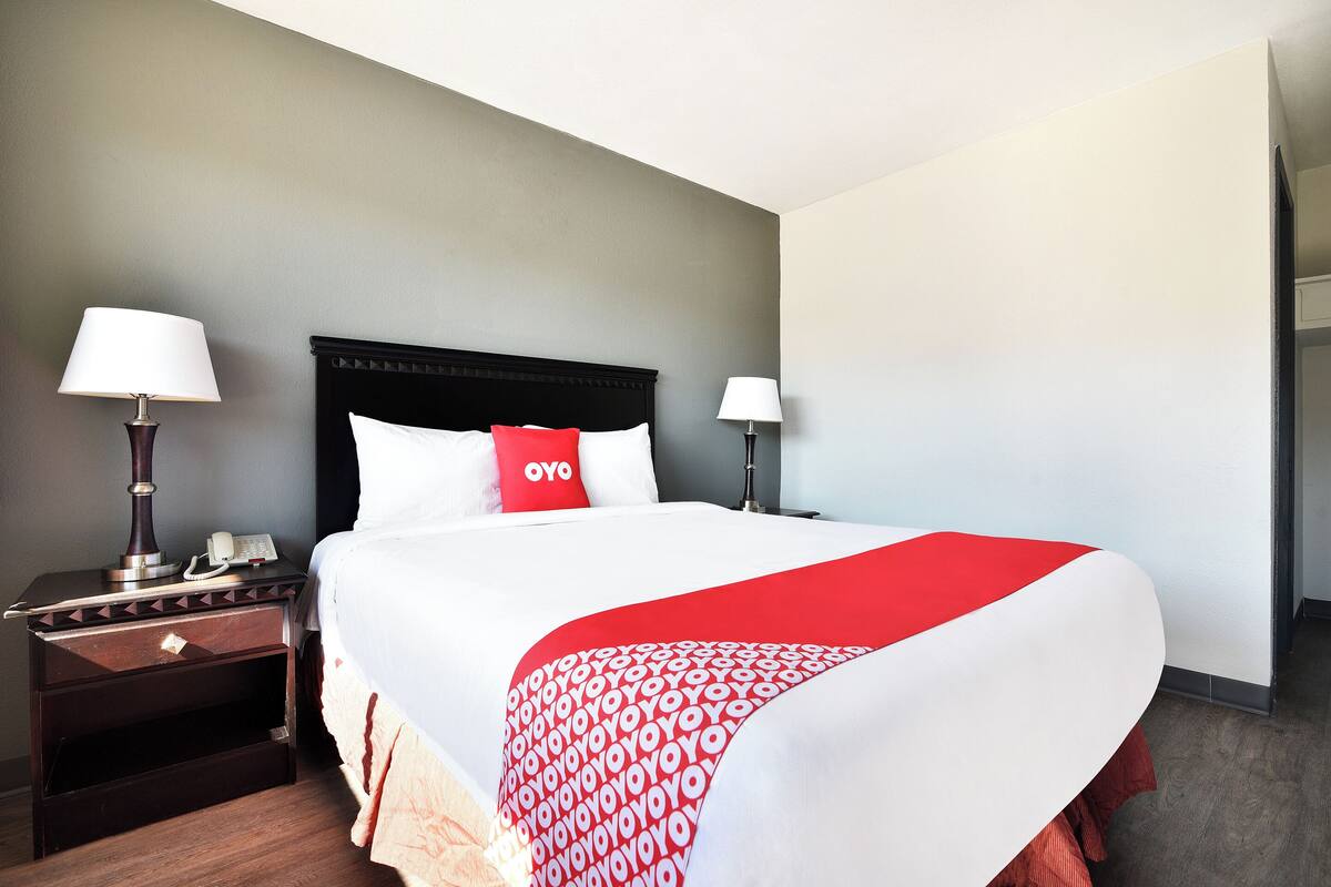 A hotel room with a bed, two bedside tables with lamps, a nightstand, and a red and white bedspread.