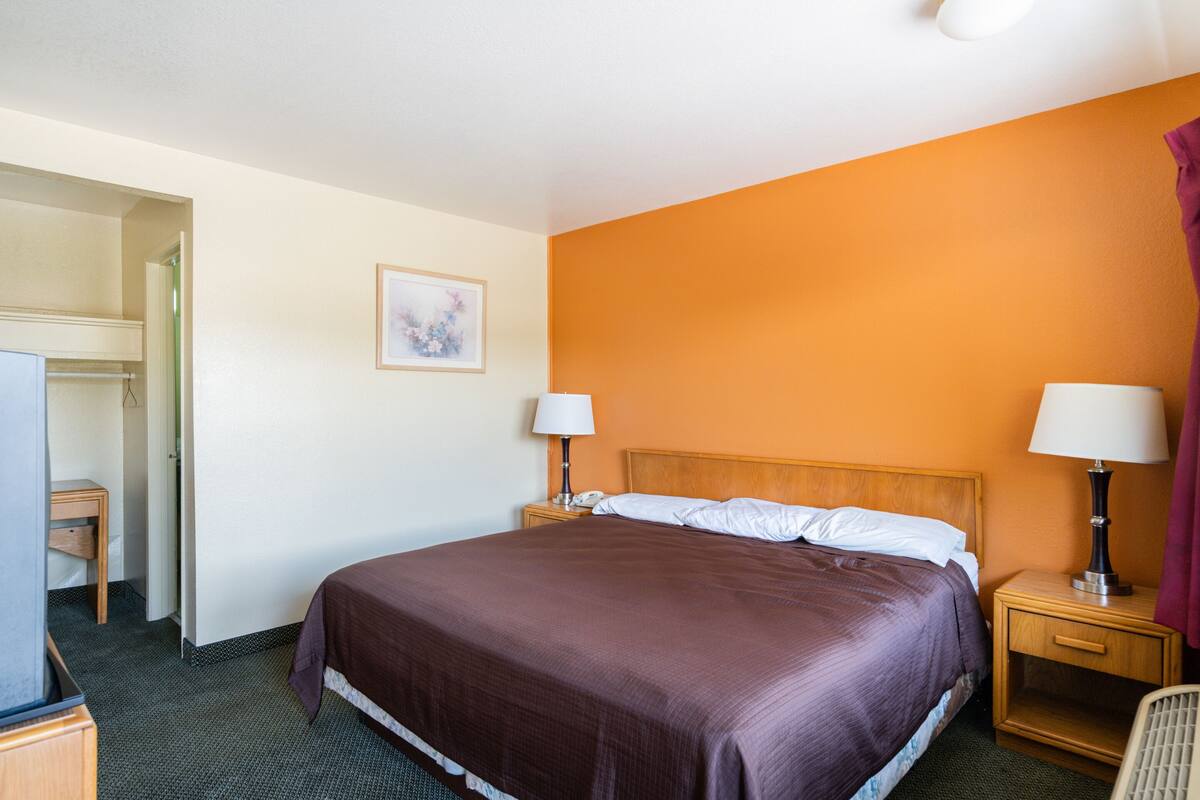 A hotel room with a large bed, two bedside tables with lamps, a wooden nightstand, a chair, and a television.