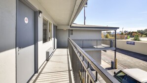 A balcony with a metal railing, a door with a '205' sign, and a view of a street with a gas station and trees in the background. - OYO Hotel Shreveport Airport North (Shreveport)