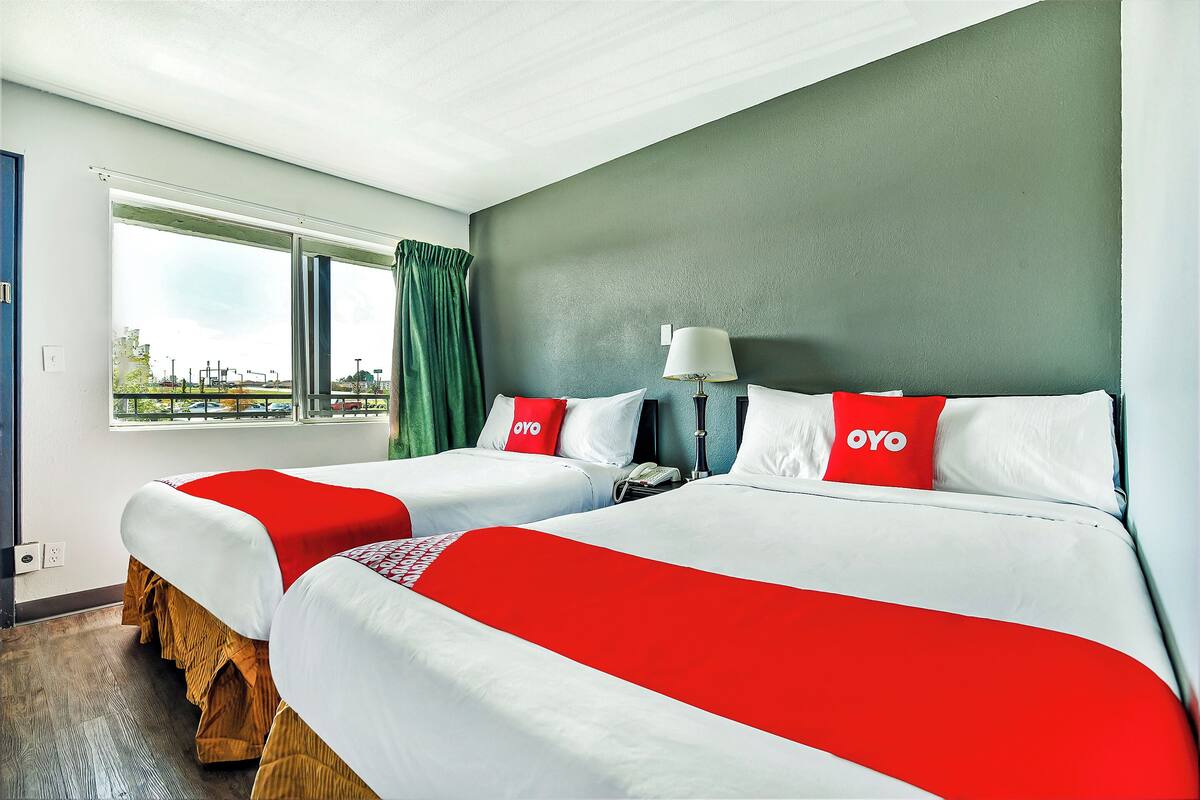 A hotel room with two beds, a window with curtains, a lamp, and a view of the outside.