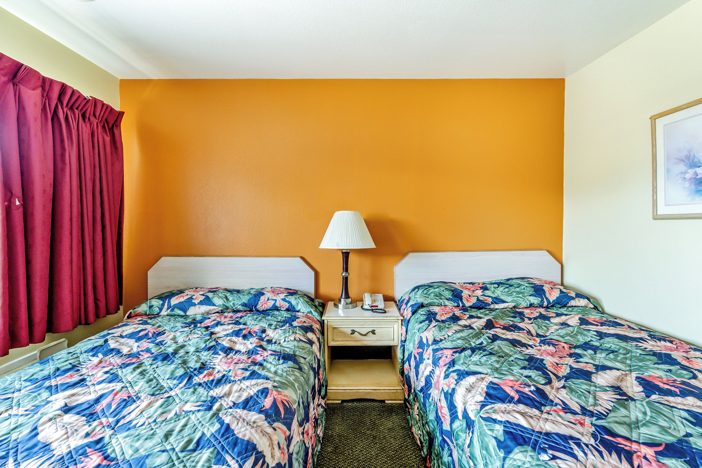 Habitación de hotel con dos camas, una mesita de noche con lámpara y una cortina roja.