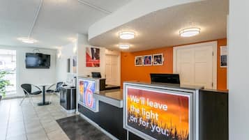 A hotel reception area with a modern design, featuring a reception desk, seating area, and a television mounted on the wall.