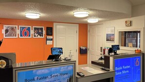 Un comptoir d’accueil d’un motel, doté d’écrans numériques affichant du contenu promotionnel, un comptoir avec un ordinateur et une porte sur la droite.