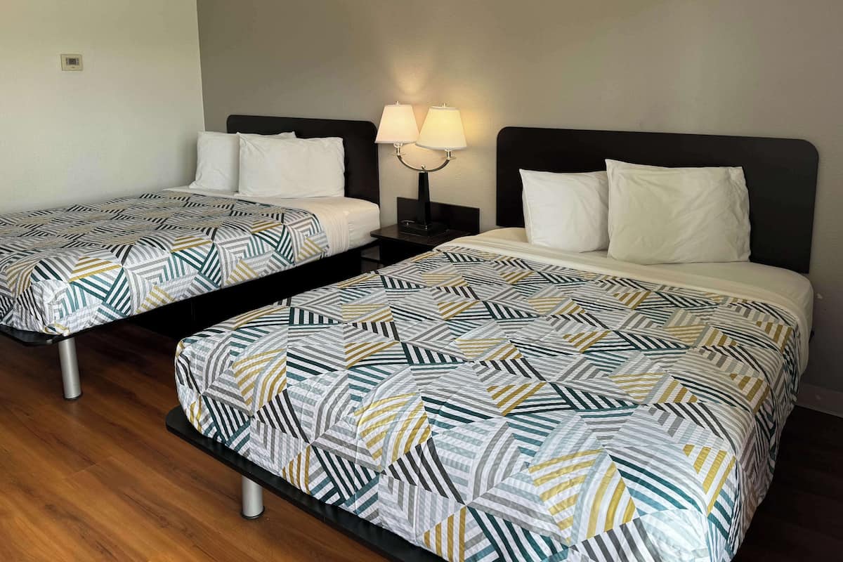 Two twin beds with geometric-patterned bedding, a bedside table with a lamp, and a wooden floor.