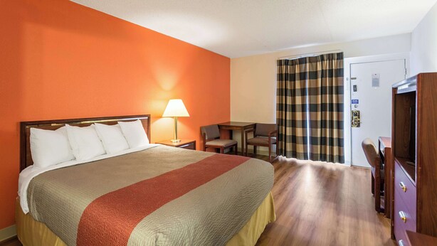 Una habitación de hotel con una cama grande, un escritorio con silla, un televisor y una puerta con cortina.