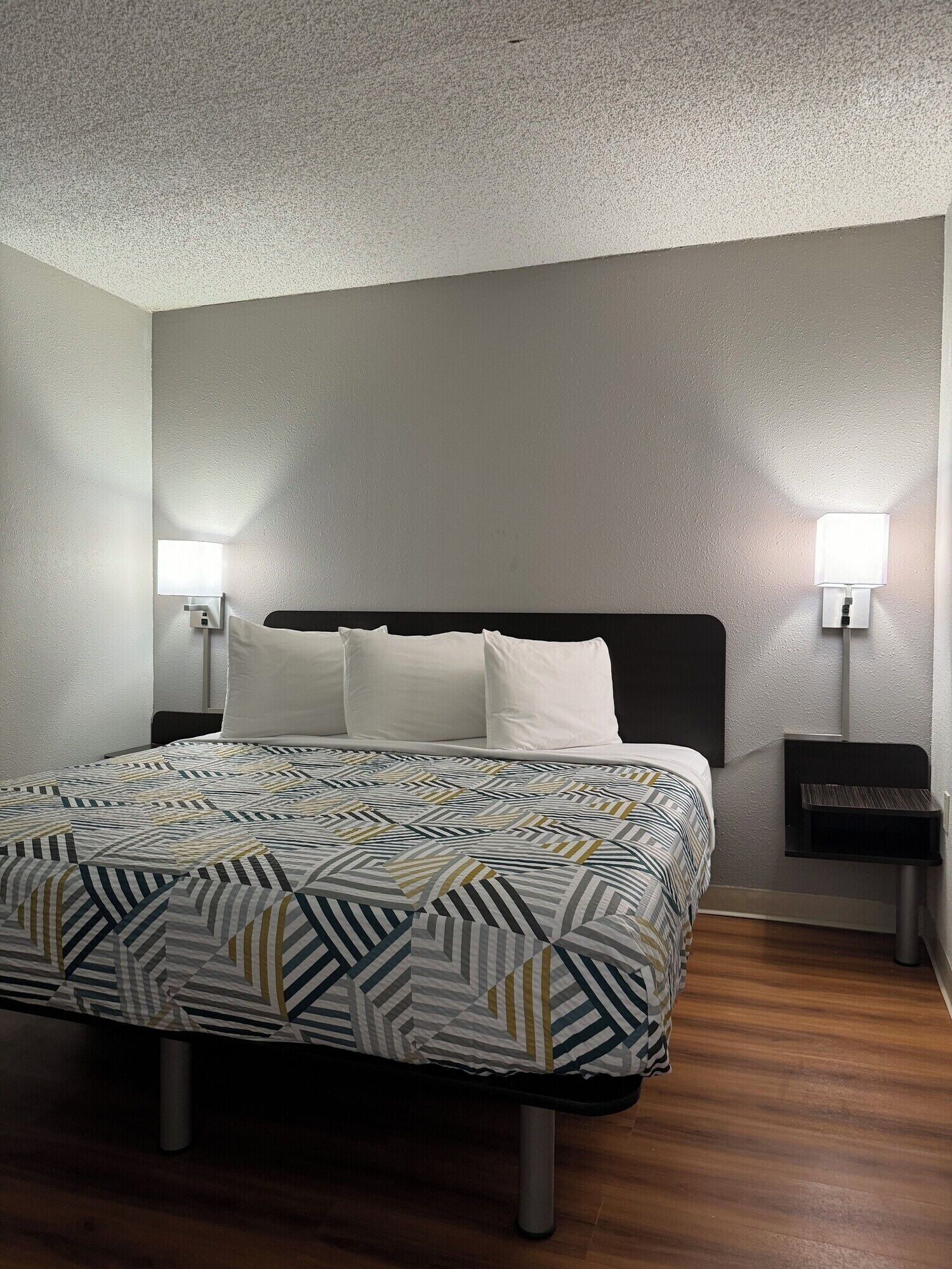 A neatly made bed with a patterned bedspread and pillows, two bedside tables with lamps, and a textured ceiling.