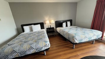 A hotel room with two single beds, a nightstand with a lamp, and a wooden floor.