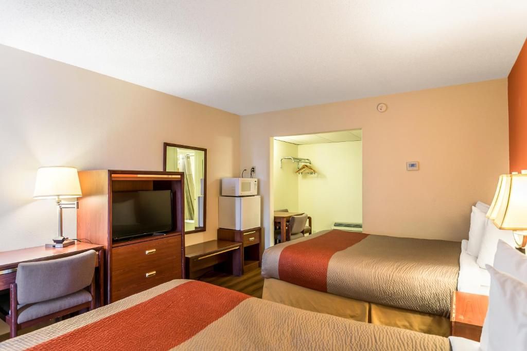 A hotel room with two beds, a desk with a television, a mirror, and a bathroom visible through an open door.