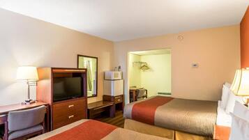 A hotel room with two beds, a desk with a television, a mirror, and a bathroom visible through an open door.