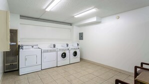 Une buanderie équipée de quatre machines à laver, d’un système de ventilation et d’un luminaire au plafond.