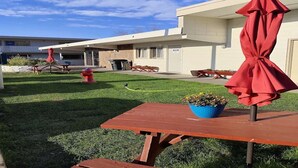 Un espace patio avec un parasol rouge, une borne d’incendie et un bac à fleurs bleu.