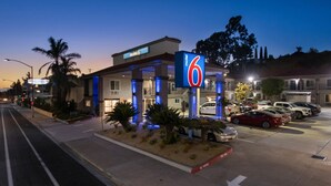 Ein Motel mit einem gut sichtbaren Schild mit der Zahl 6, einem Parkplatz mit mehreren Autos und einem gut beleuchteten Eingang.