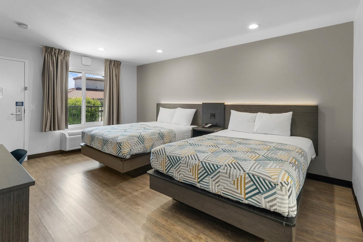 Quarto de hotel moderno com duas camas, uma varanda e uma secretária.