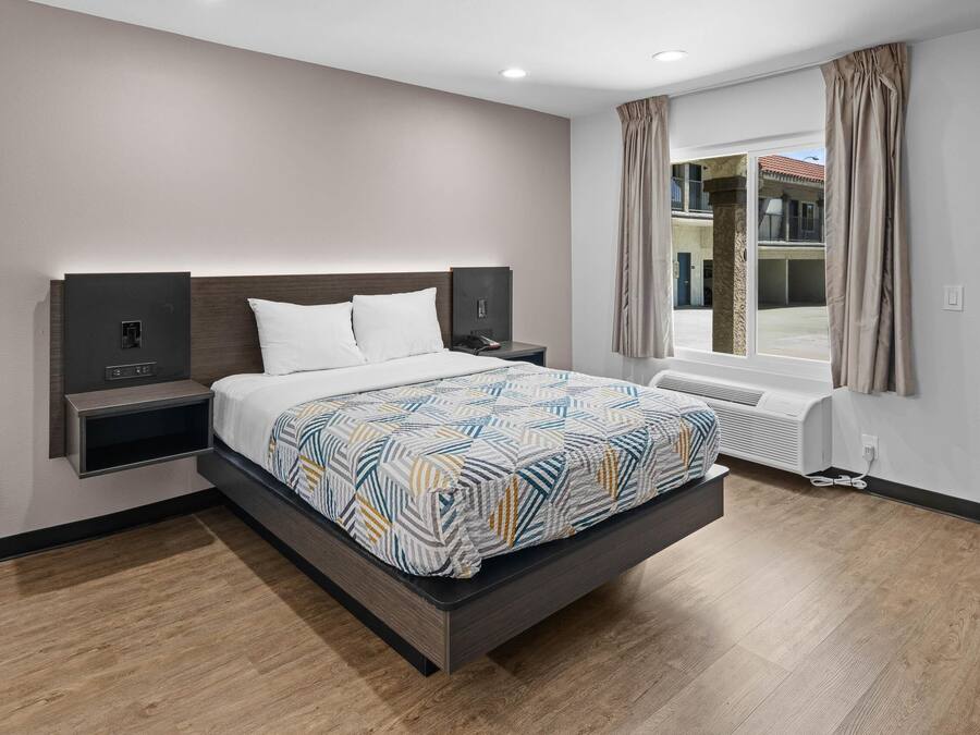 Quarto de hotel moderno com cama grande, mesas de cabeceira, aquecedor e vista para o exterior.