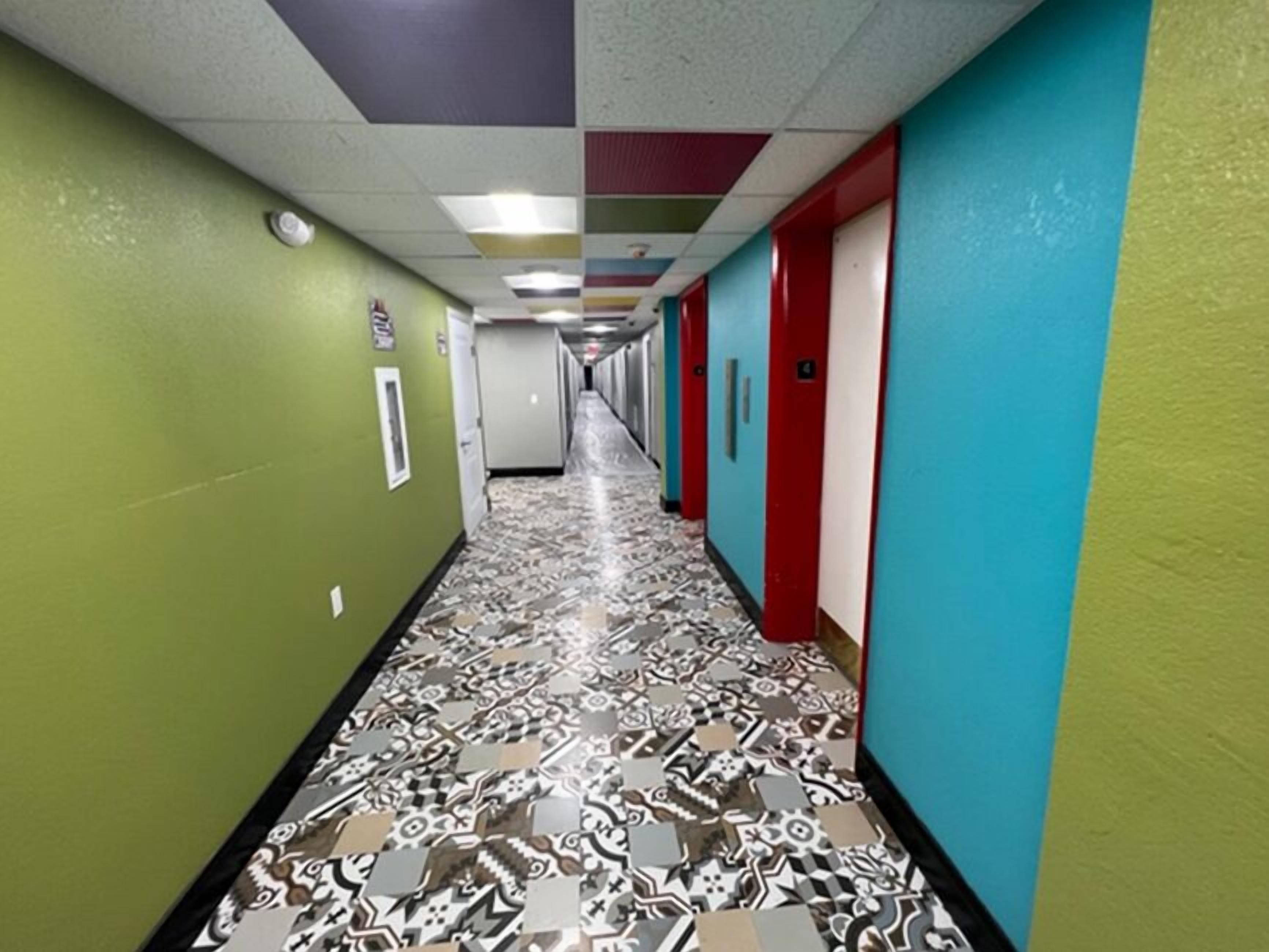 Um corredor com piso estampado, paredes verdes e azuis, e portas com detalhes em vermelho e branco.