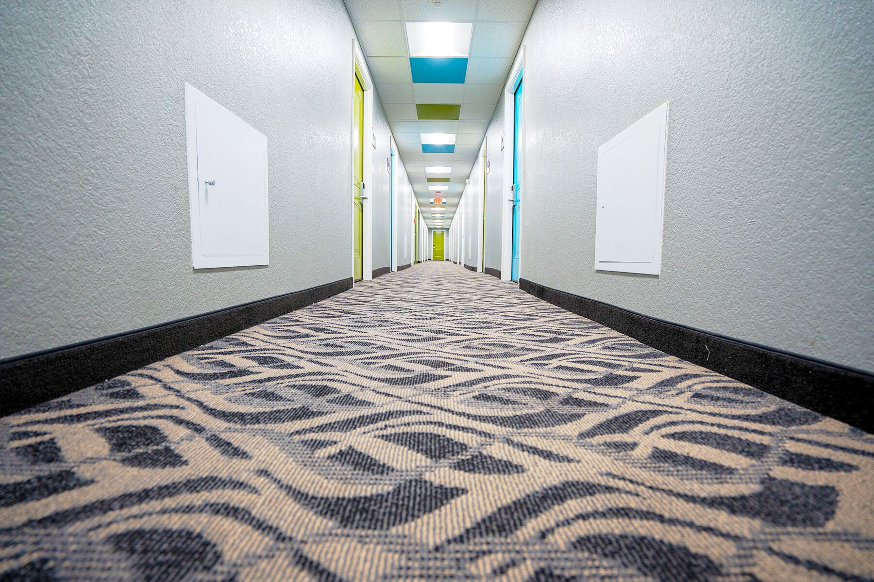 A hotel hallway with patterned carpet, white walls, and doors with light-colored panels.