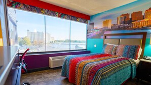 A bedroom with a large window, a bed with a colorful blanket, a desk, and a chair. - Philly Inn & Suites (Philadelphia)