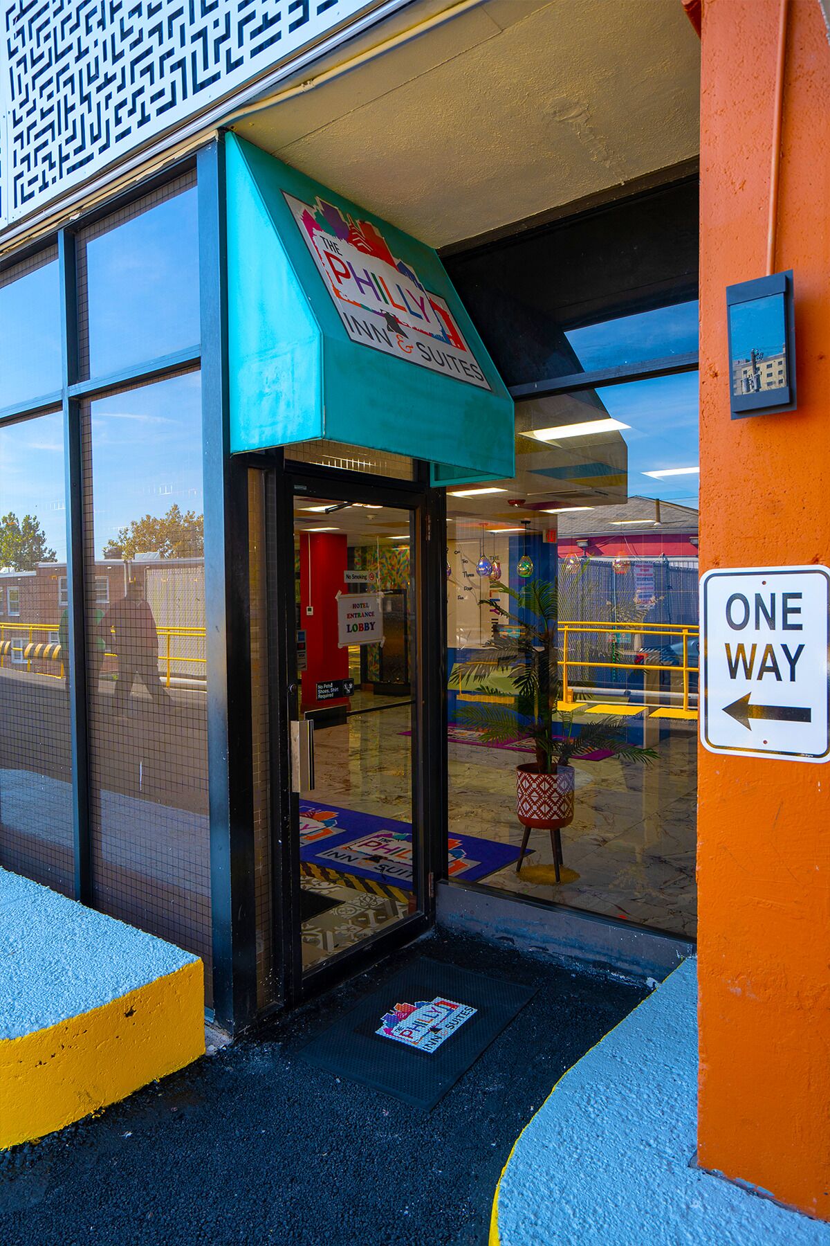 A hotel entrance with a teal awning, glass doors, and a 'One Way' sign.