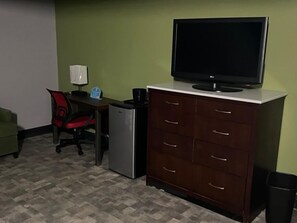 A room with a desk, chair, television, refrigerator, and a cabinet.