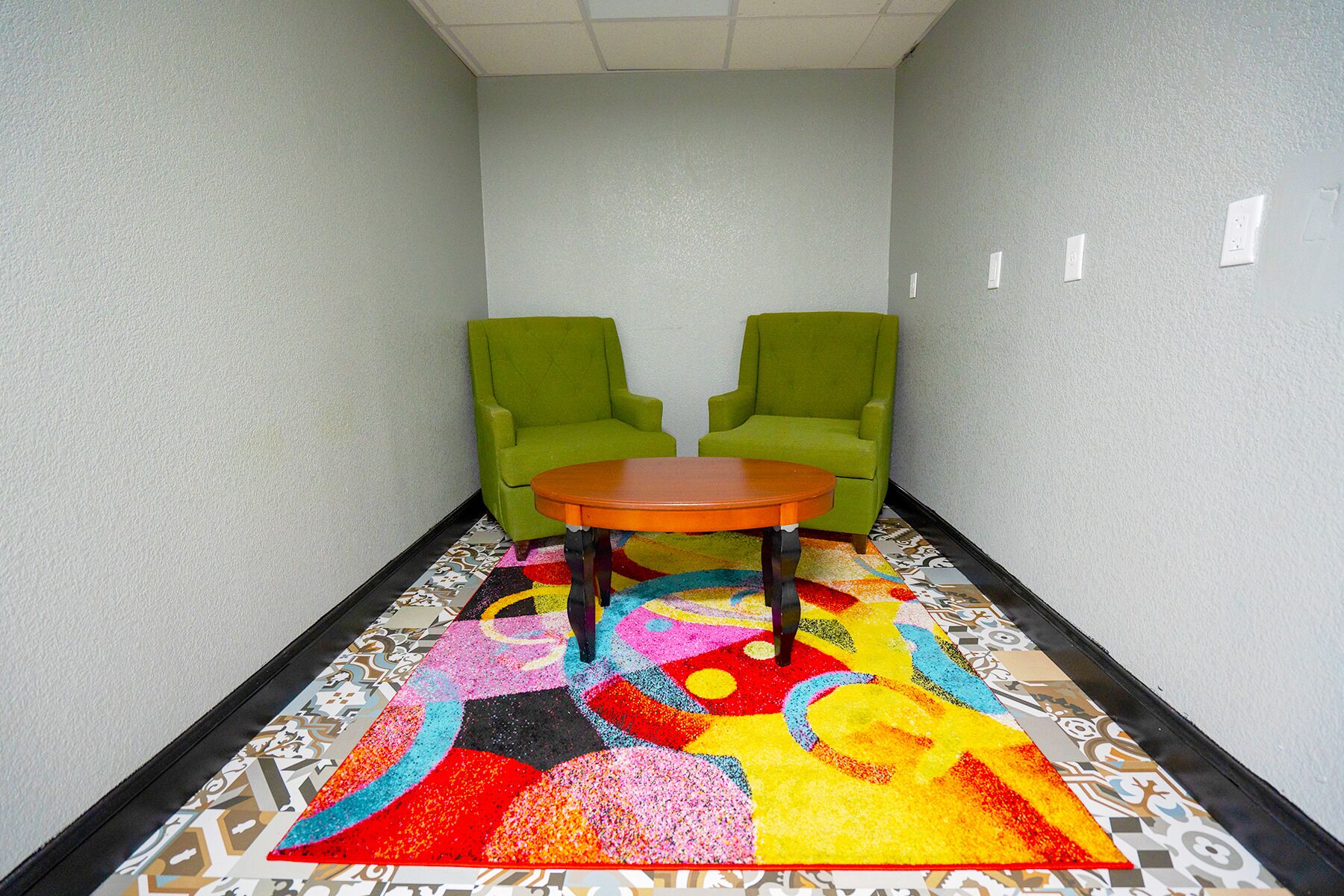 Un pasillo con dos sillones verdes y una mesita redonda, cubierto con un colorido estampado geométrico.