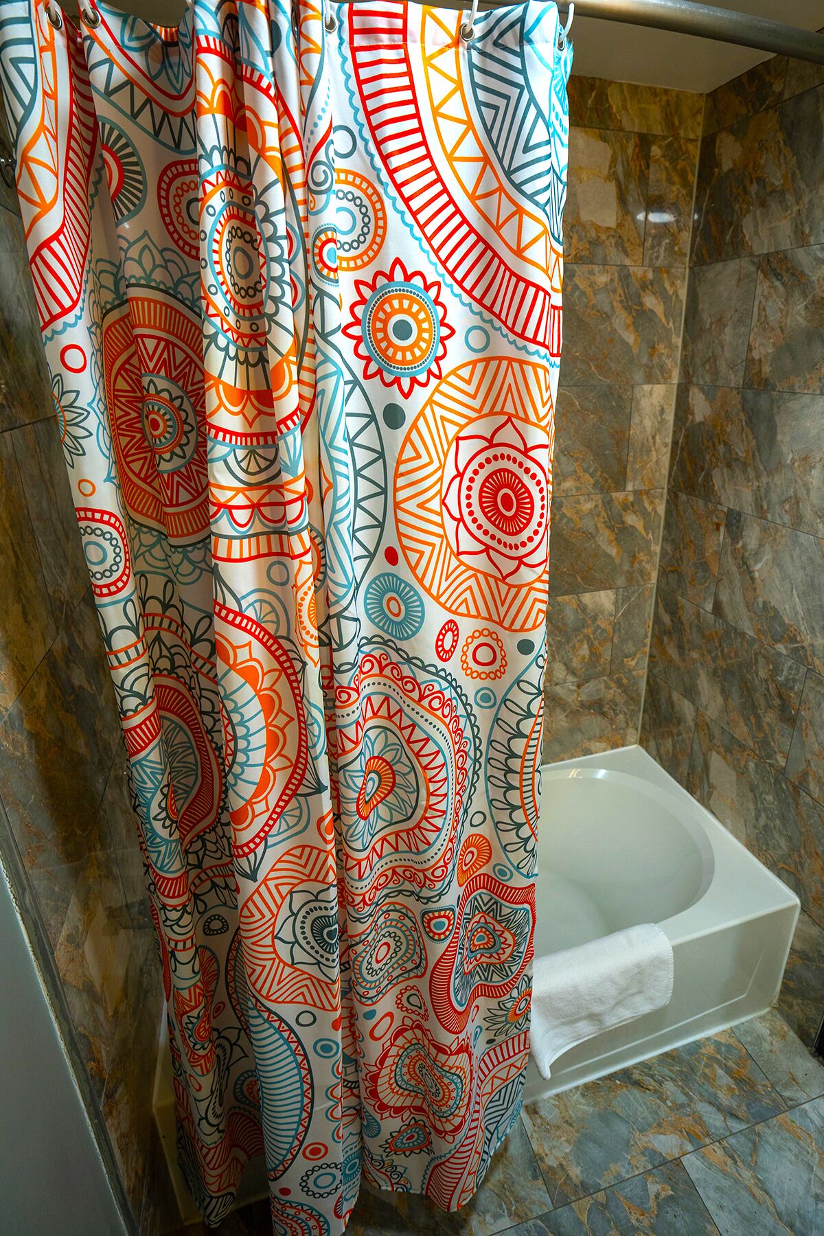 Un baño con cortina de ducha de estampado paisley colorido, una bañera blanca y suelo de mármol.