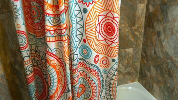 Un baño con cortina de ducha de estampado paisley colorido, una bañera blanca y suelo de mármol.