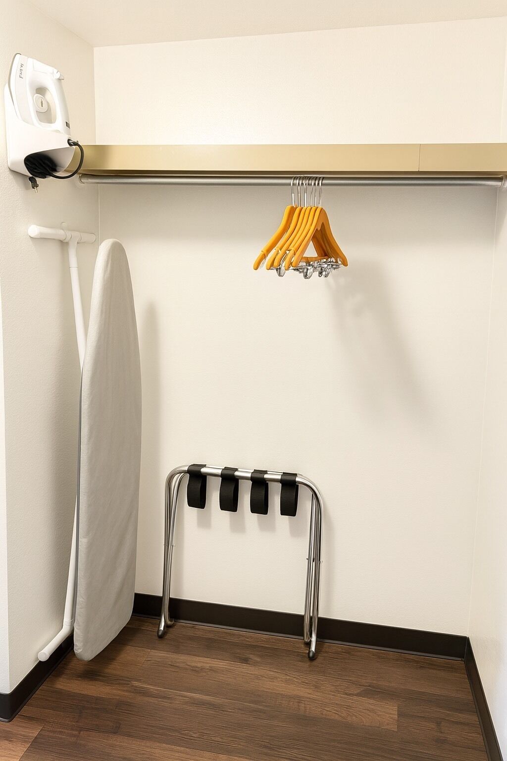 A corner of a room with a wooden floor, a white radiator, a hanging clothes rack with yellow handles, and a white iron.