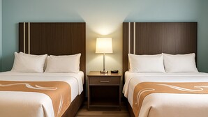 A hotel room with two beds, a nightstand with a lamp, and a wooden floor. - Village Inn & Suites  (Sarnia)