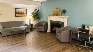 A living room with a fireplace, a sofa, a chair, and a desk with a chair. - Village Inn & Suites  (Sarnia)
